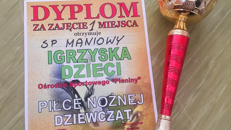 Zbliżenie na złoty puchar sportowy z czerwonym trzonem oraz pamiątkowy dyplom za zajęcie I miejsca w zawodach piłki nożnej dziewcząt w Maniowach, data 05.05.2026 r..jpg