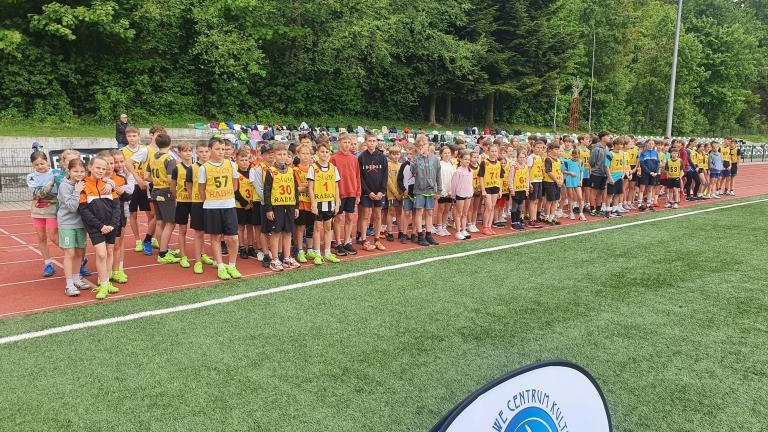 Grupa uczestników zawodów w żółtych znacznikach sportowych na bieżni lekkoatletycznej.