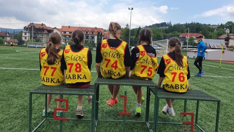Zawodniczki w żółtych znacznikach startowych siedzące tyłem na podium.