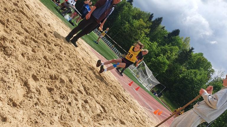 Moment skoku w dal nad piaskownicą podczas zawodów sportowych.