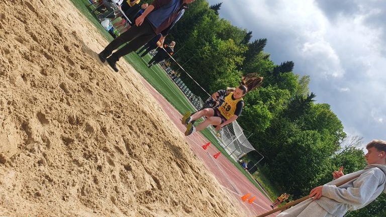 Moment skoku w dal nad piaskownicą podczas zawodów sportowych.