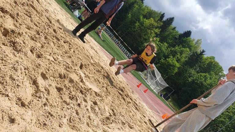 Moment skoku w dal nad piaskownicą podczas zawodów sportowych.
