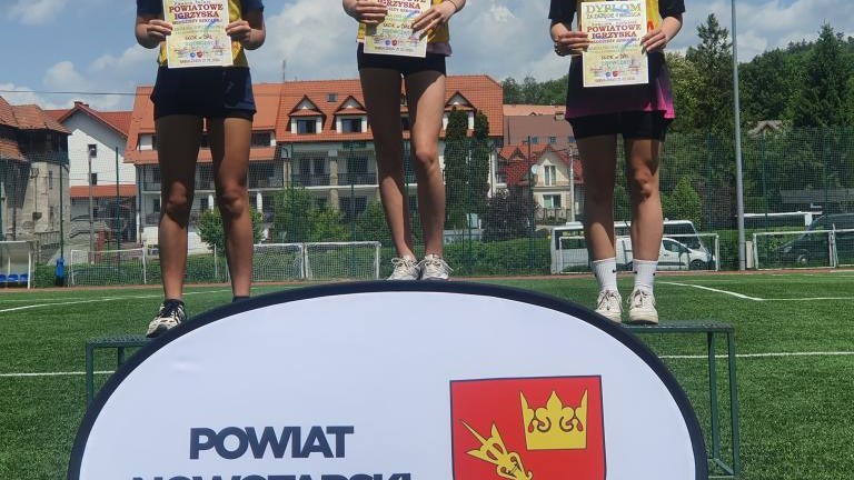 Ceremonia dekoracji – trzy uśmiechnięte zawodniczki prezentują zdobyte dyplomy na podium.