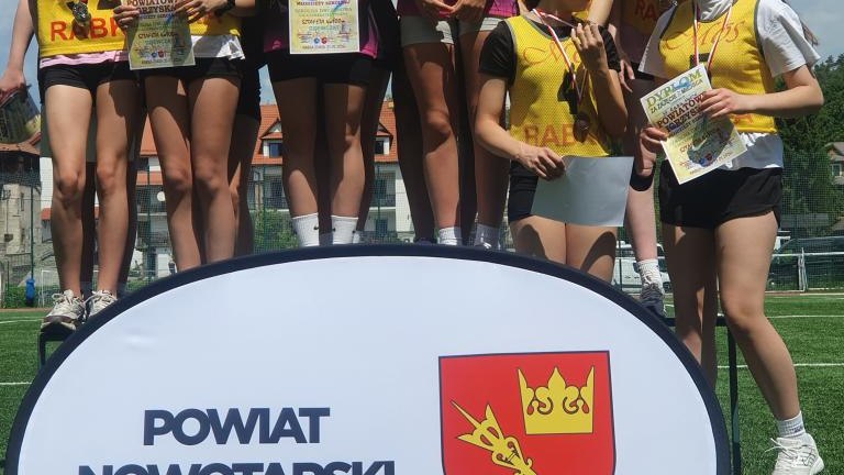 Pamiątkowe zdjęcie grupowe zawodniczek w żółto-czarnych strojach startowych świętujących sukces na podium.
