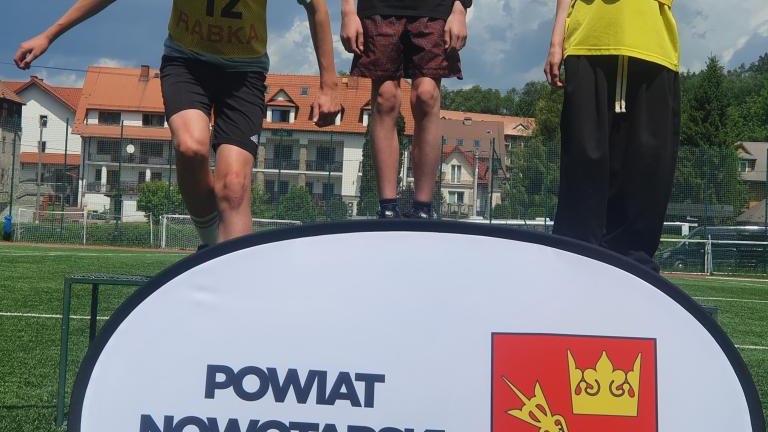 Trzej zawodnicy w sportowych strojach na podium podczas ogłoszenia wyników konkurencji.